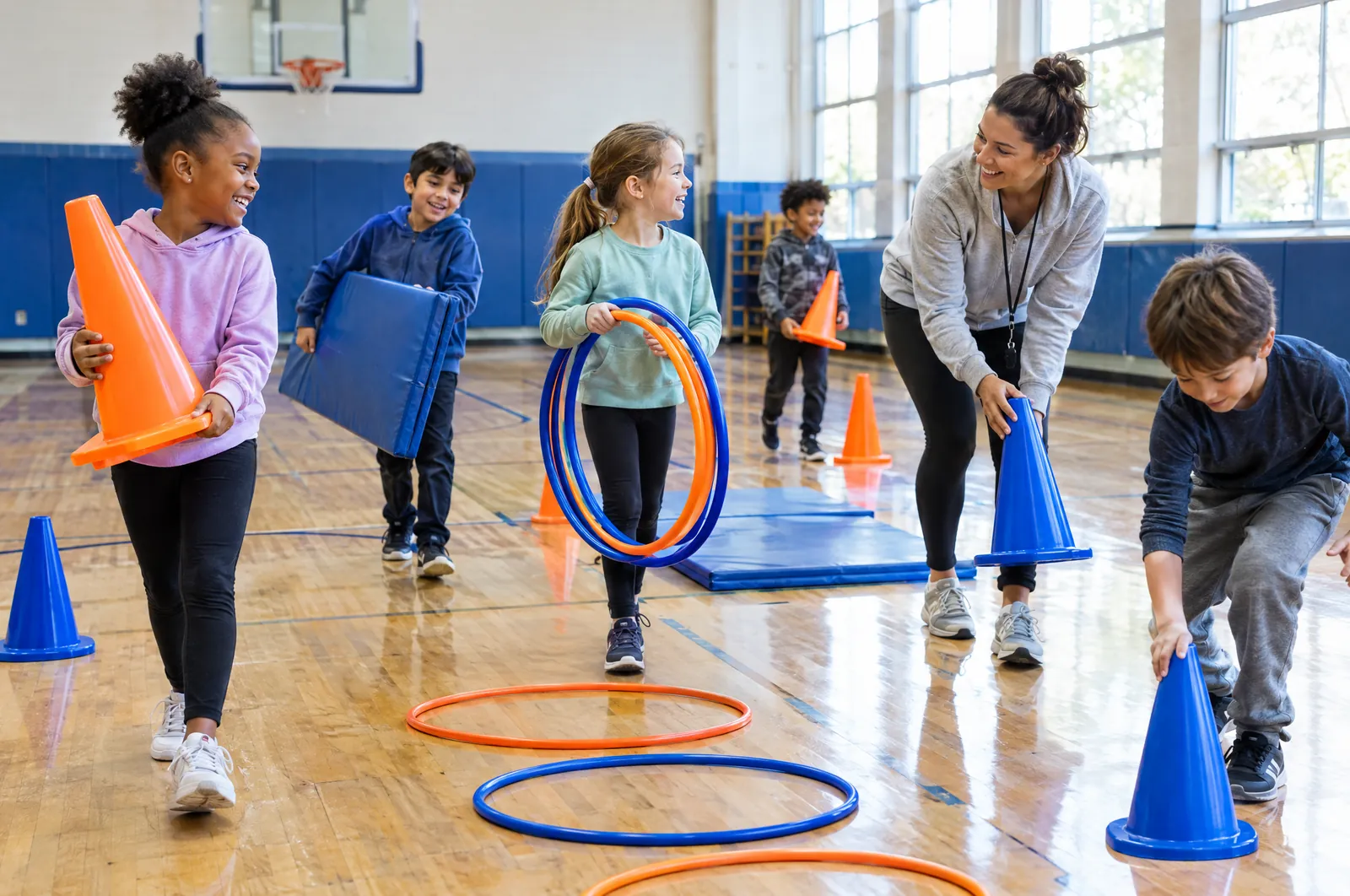 Des élèves installent un parcours actif avec cônes et cerceaux dans le gymnase